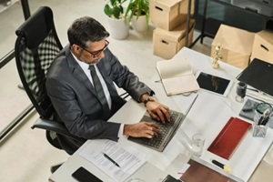 mature chief executive officer or owner of notary firm typing on laptop keyboard while sitting by desk during organization of work