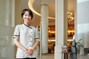 cheerful young Asian hotel manager standing at entrance doors and smiling at camera