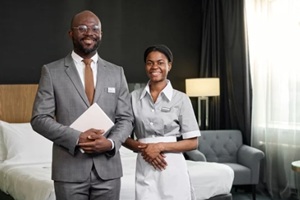 portrait of two smiling Black people as hospitality service crew looking at camera standing in hotel room copy space