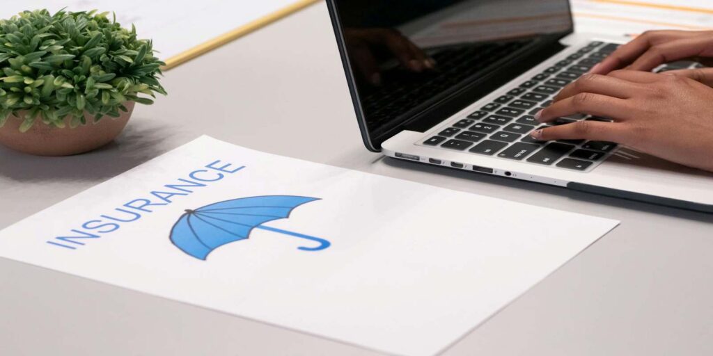 A Paper with Insurance Sign Besides A Person Typing on Laptop