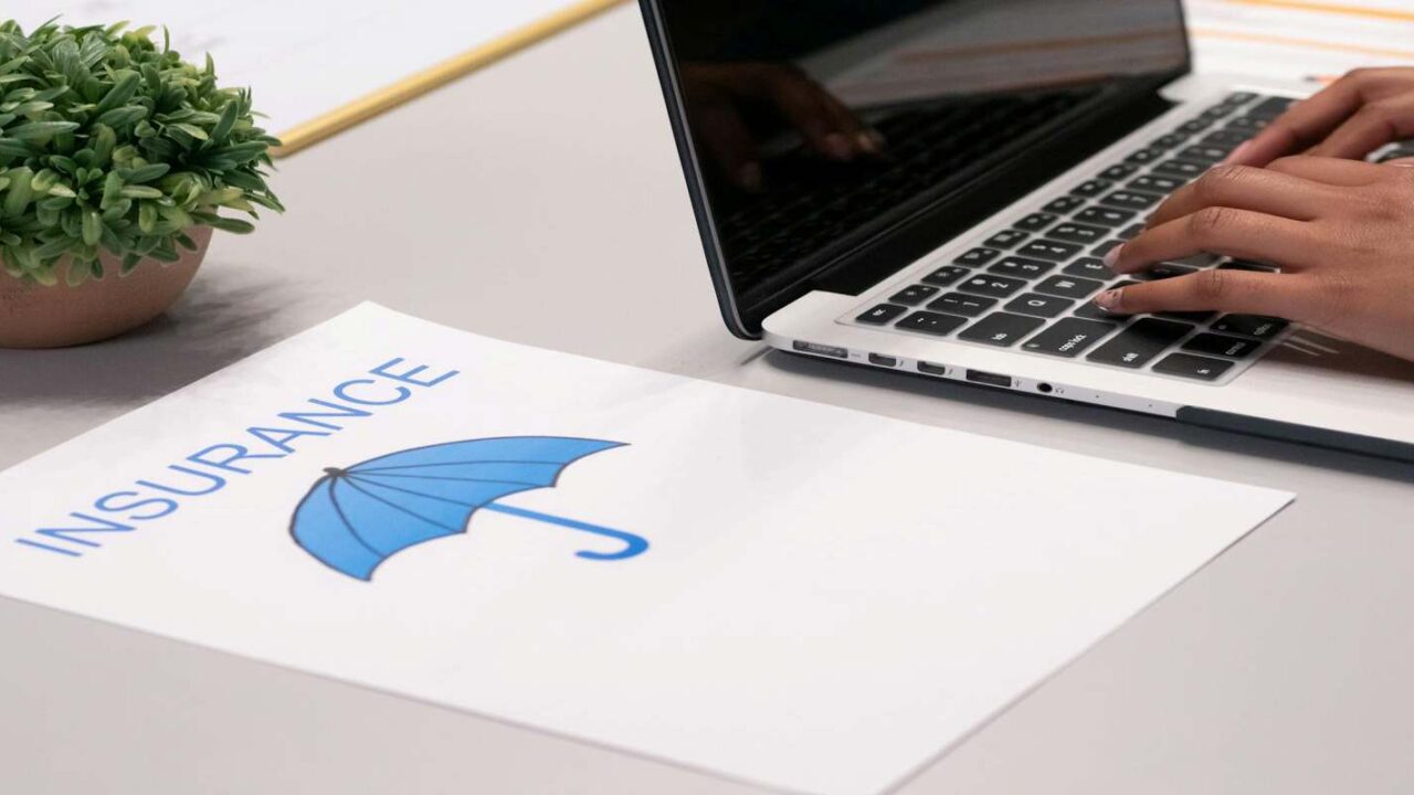 A Paper with Insurance Sign Besides A Person Typing on Laptop