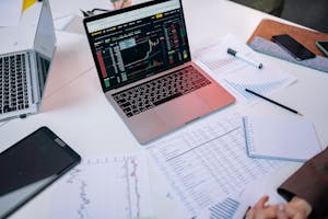 Data Appearing on Laptop Screen Surrounded by Papers