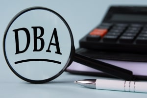 DBA Written on Magnifying Glass with Pen Notepad and Calculator