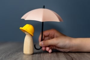 Hand Holding Umbrella Over Wooden Doll Worker and Employee Insurance Concept